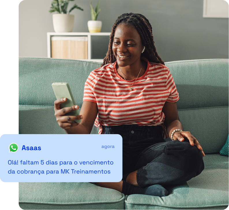 Mulher sentada no sofá olhando para a tela do celular que exibe uma notificação de vencimento de uma cobrança para MK Treinamentos